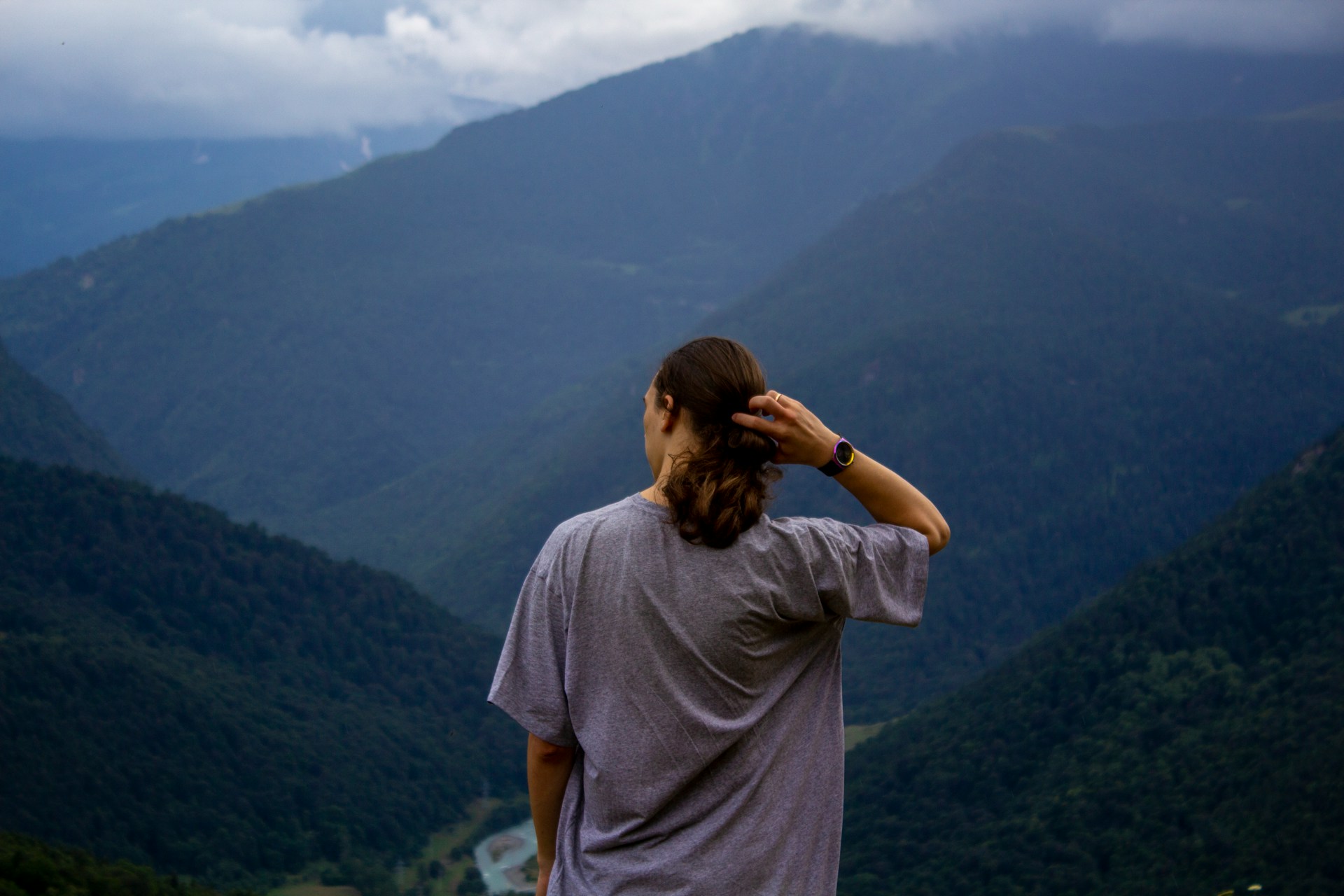 a man looking out over a mountain range with his hand in his hair and wearing a black watch